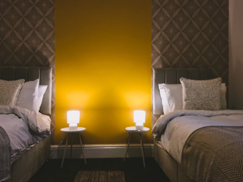 Modern bedroom with two single beds, yellow accent wall, bedside lamps, and patterned wallpaper