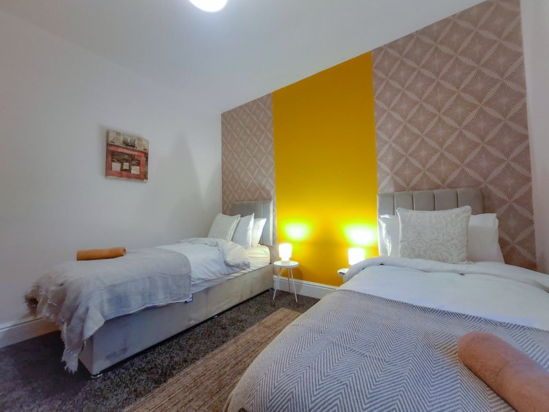 Modern bedroom with two single beds, yellow accent wall, patterned wallpaper, and bedside lighting