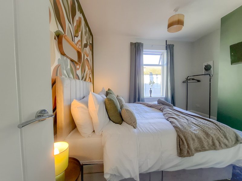 Modern bedroom with double bed, multiple pillows, green accent wall and natural light