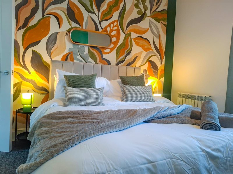 Modern bedroom with double bed, green headboard, colorful leaf artwork and warm lighting