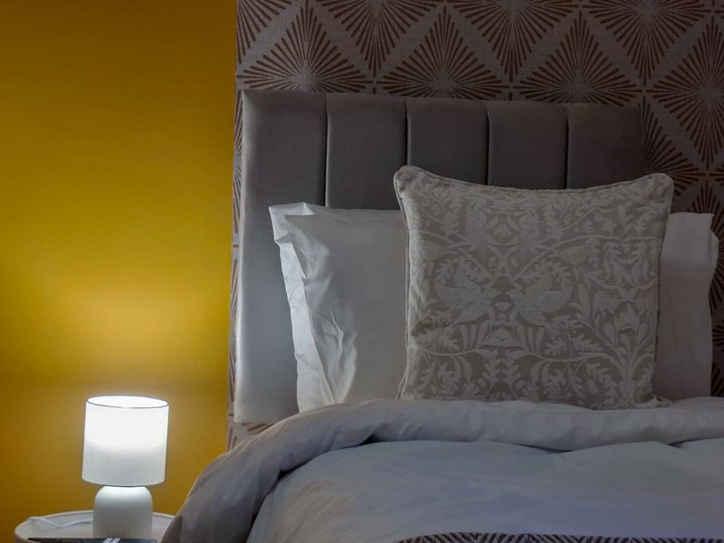 Modern bedroom with padded headboard, patterned pillows, blue bedding and bedside lamp
