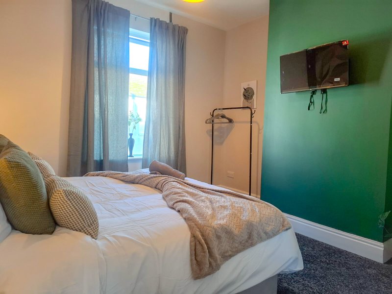 Bedroom with double bed, green accent wall, TV, and window with curtains