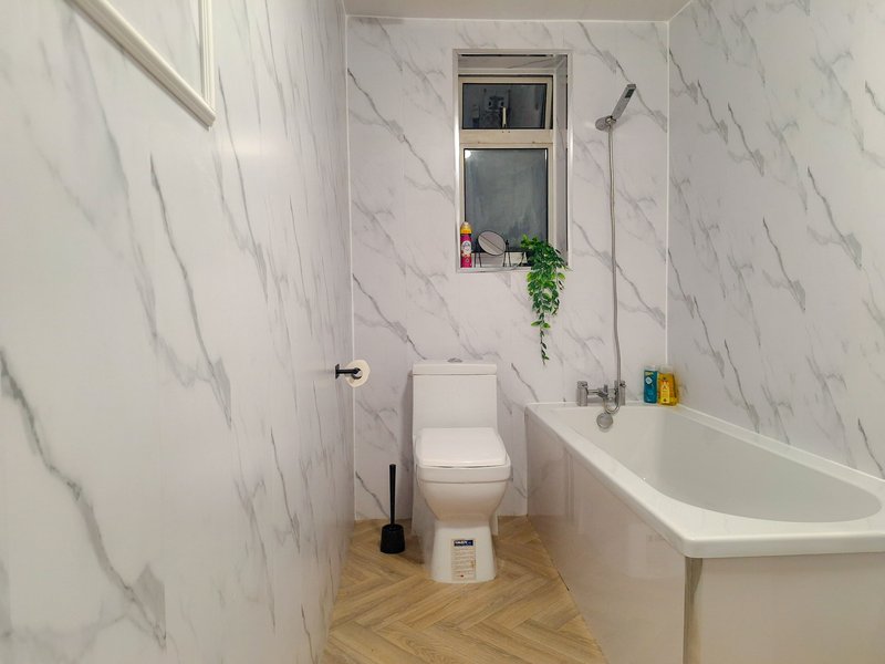 Modern bathroom with marble-effect tiles, toilet, bathtub, window with potted plant and toiletries on shelf