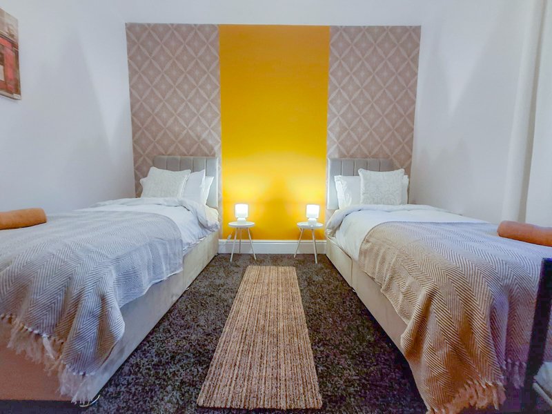 Twin bedroom with two single beds, yellow headboard feature, patterned wallpaper and striped rug