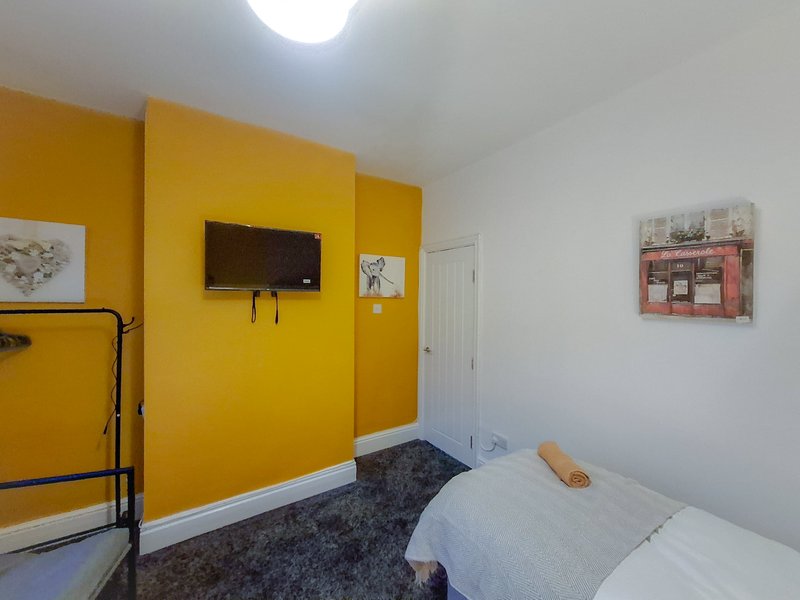 Bedroom with yellow accent wall, mounted TV, bed, and dark carpet flooring