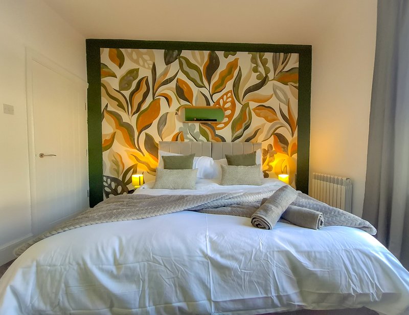 Bedroom with double bed, decorative leaf-pattern headboard, warm bedside lamps and white bedding