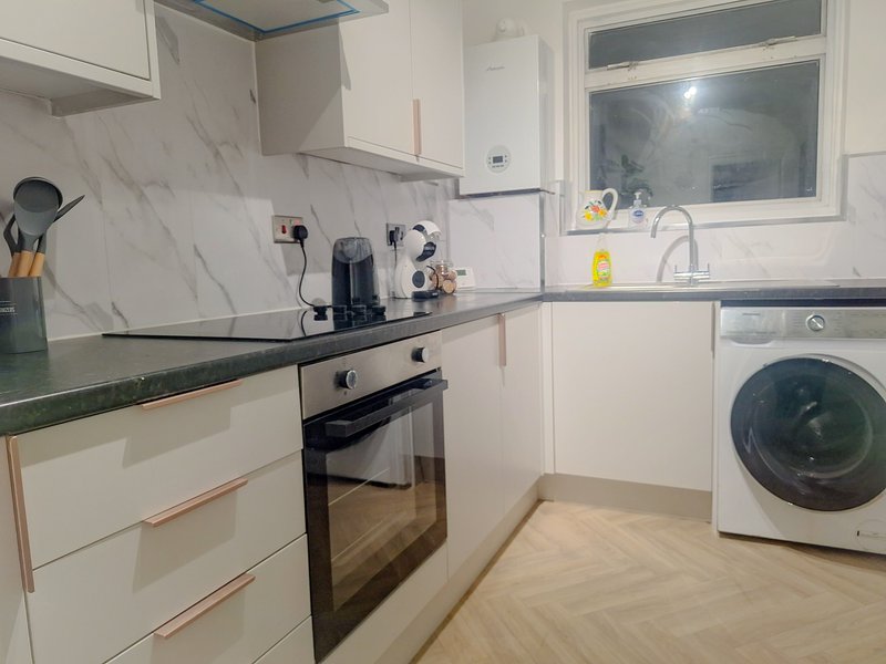 Modern kitchen with white cabinetry, marble backsplash, built-in oven and integrated washing machine