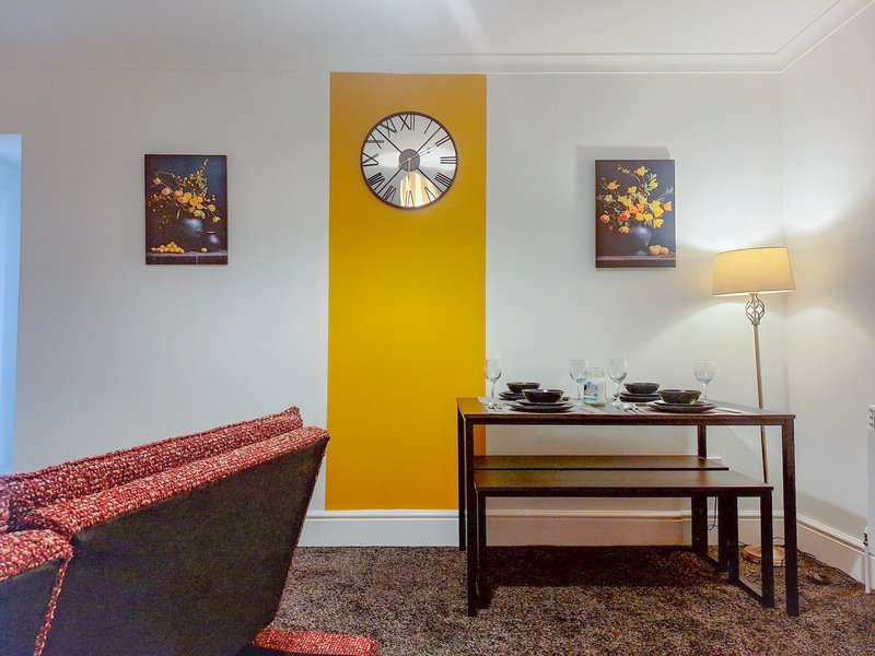 Modern living room with red sofa, yellow accent wall, clock, wooden dining table and floor lamp