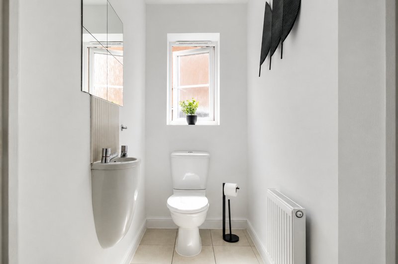 Modern bathroom with white walls, toilet, sink, mirror and window with natural light