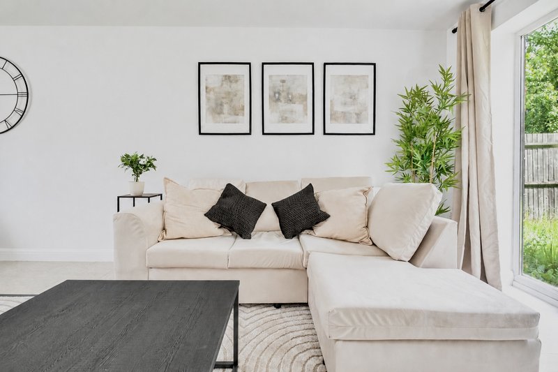 Bright living room with cream L-shaped sofa, black cushions, framed wall art, and garden view