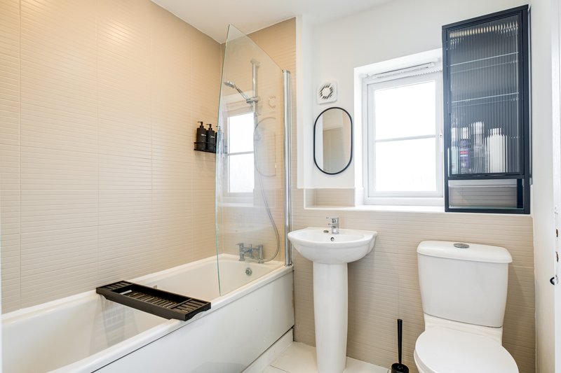 Modern bathroom with bathtub, pedestal sink, toilet, and window