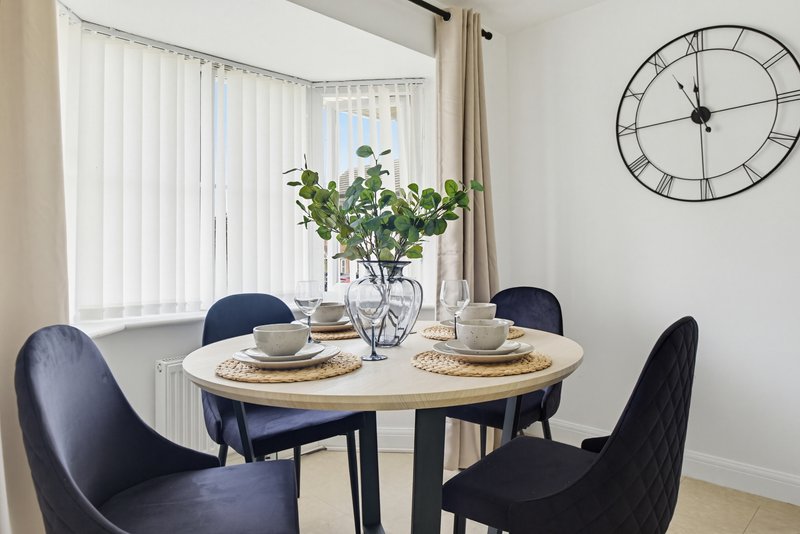 Dining area with round wooden table, four black chairs, and fresh flowers in vase