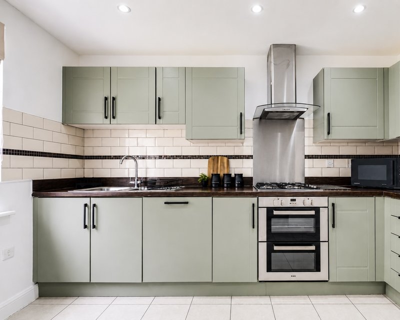 Modern kitchen with sage-green cabinetry, black countertops, white subway tile backsplash, and integrated appliances