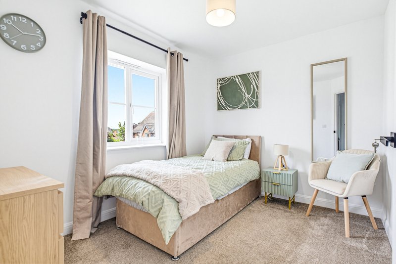 Bright bedroom with single bed, wooden furniture, armchair and window overlooking residential street