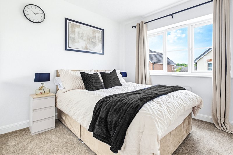 Bright bedroom with double bed, white bedding, black cushions, and large window with countryside view