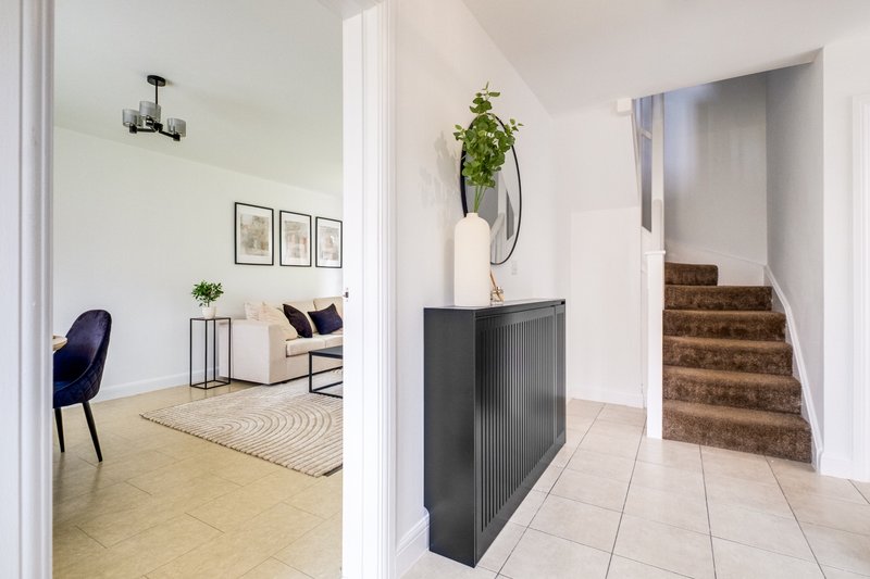 Bright hallway with stairs, dark console table, hanging plant, and open living area beyond