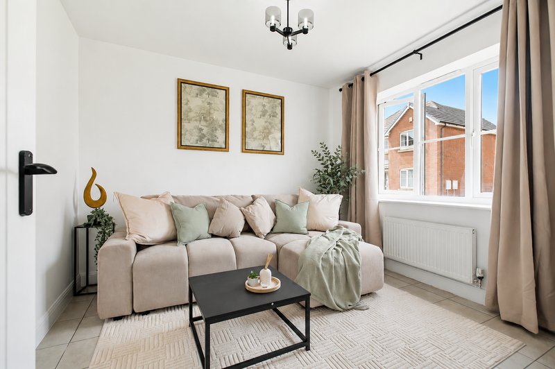 Bright living room with beige sofa, black coffee table, framed wall art and large windows overlooking street
