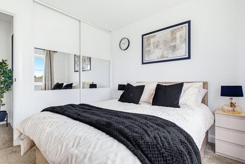 Modern bedroom with double bed, white bedding, black throw, mirrored wardrobe and framed wall art