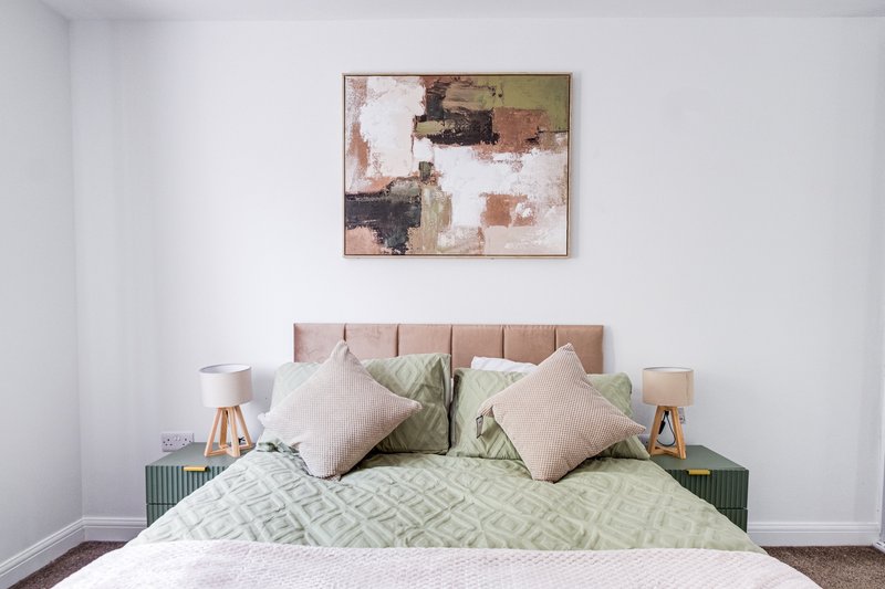 Bedroom with upholstered headboard, green bedding, decorative pillows and abstract wall art