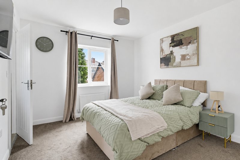 Bright bedroom with double bed, green bedding, wall art, clock and garden view from window