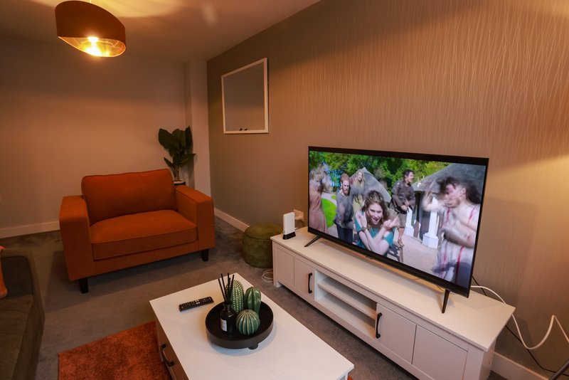 Modern living room with orange sofa, white TV stand, ceiling lamp and textured walls
