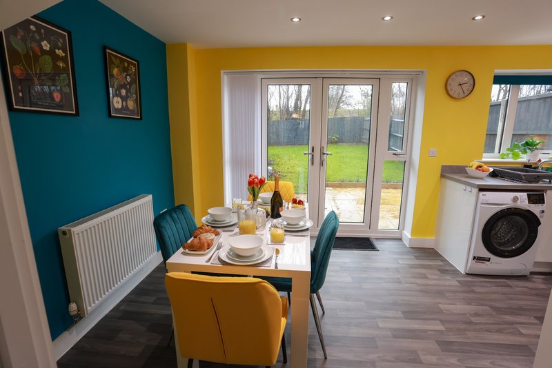 Modern kitchen-diner with teal and yellow walls, dining table set for meal, garden doors and washing machine