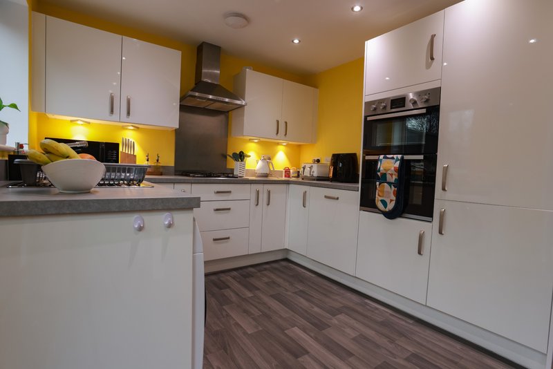 Modern kitchen with white cabinets, yellow accent wall, built-in appliances and dark wood-effect flooring