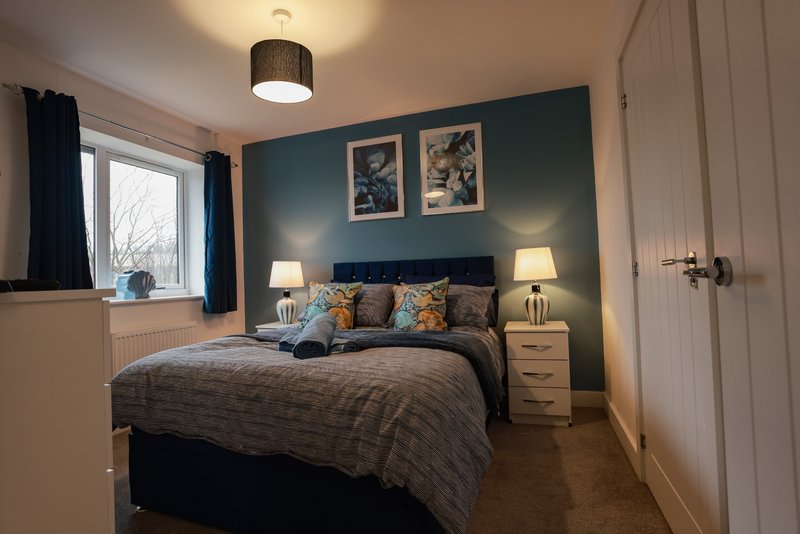 Modern bedroom with double bed, teal accent wall, bedside lamps and framed artwork