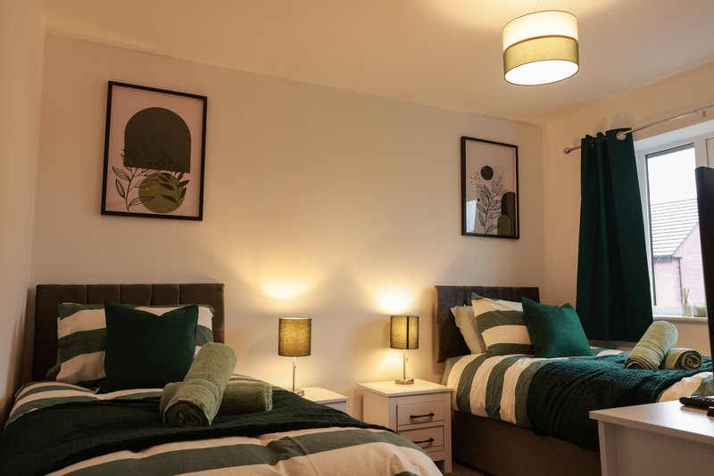 Twin bedroom with black headboards, green and cream bedding, bedside lamps and framed wall art