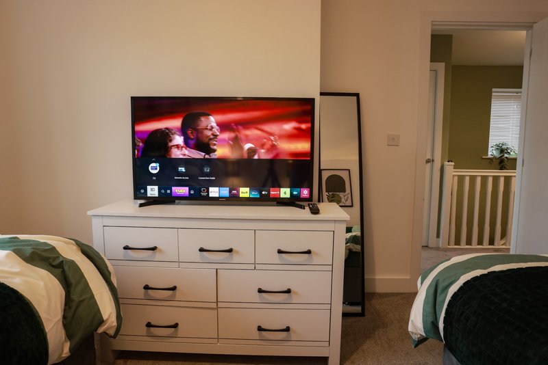Bedroom with white dresser, wall-mounted TV, and two beds with green bedding