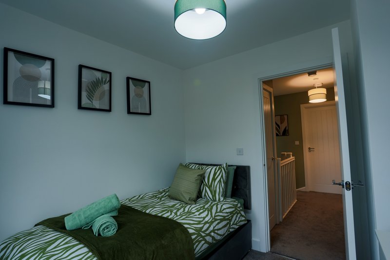Bedroom with single bed, zebra-print bedding, green pillows, framed wall art and ceiling light