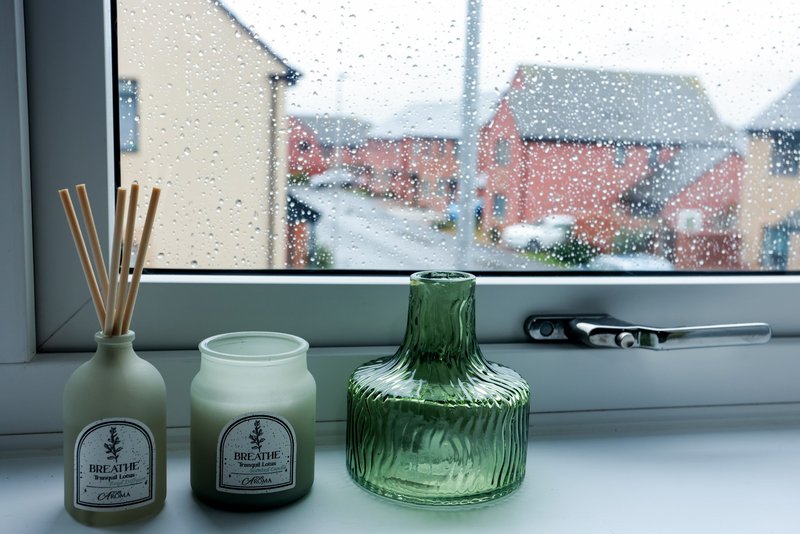 Windowsill with candles and glass vase, rainy day view of brick houses outside