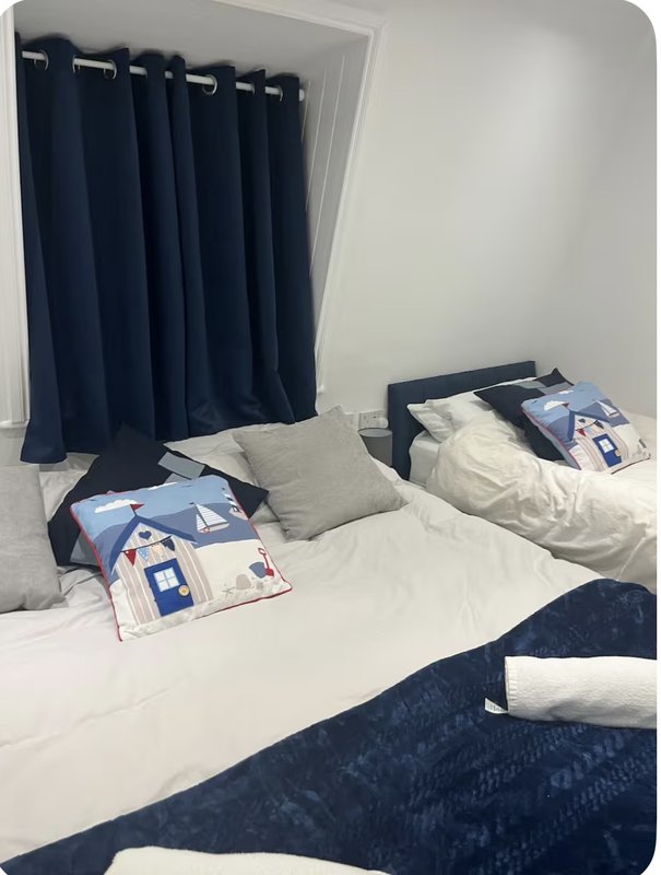 Bedroom with two single beds, white bedding, blue curtains, and grey cushions