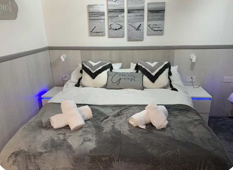 Modern bedroom with grey upholstered bed, white pillows, patterned cushions, and framed coastal artwork
