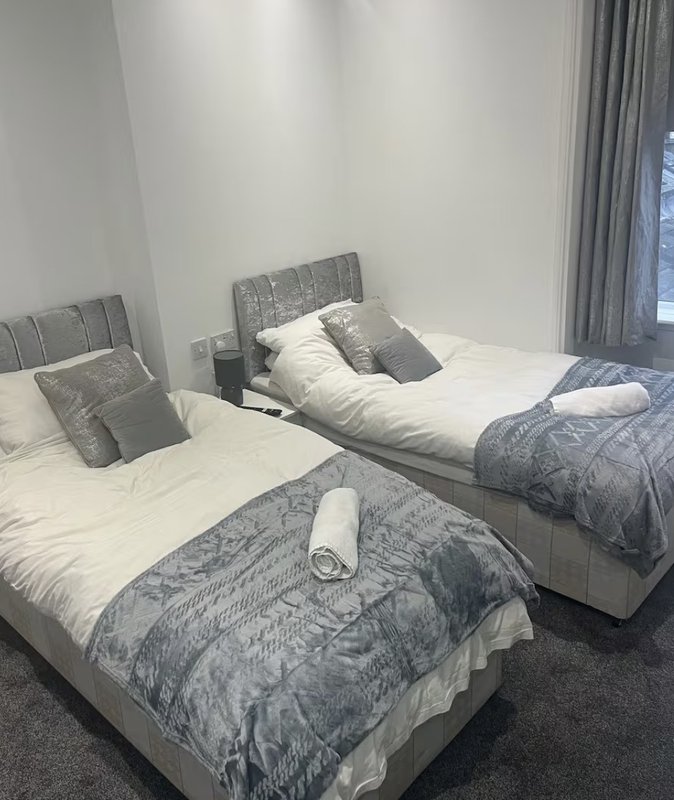 Bedroom with three single beds, grey upholstered headboards, and floor-to-ceiling curtains