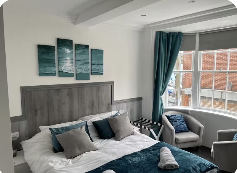 Modern bedroom with double bed, grey headboard, teal artwork, and seating area by window