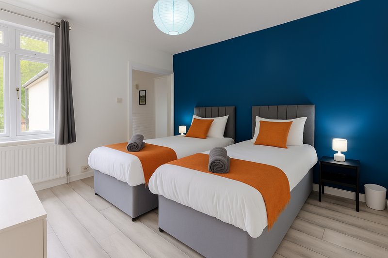 Modern twin bedroom with two beds, orange blankets, dark blue accent wall and pendant light