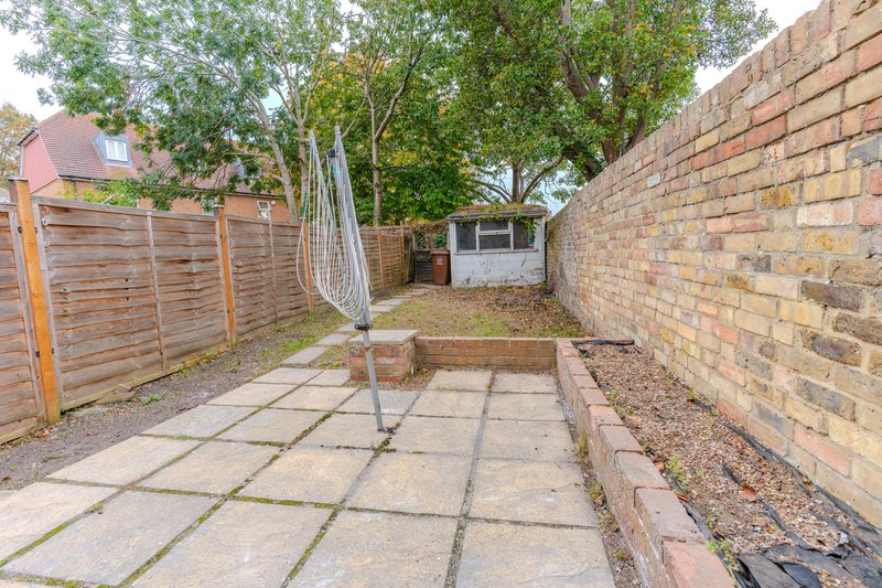 Narrow garden courtyard with paved pathway, brick walls, wooden fence and mature trees