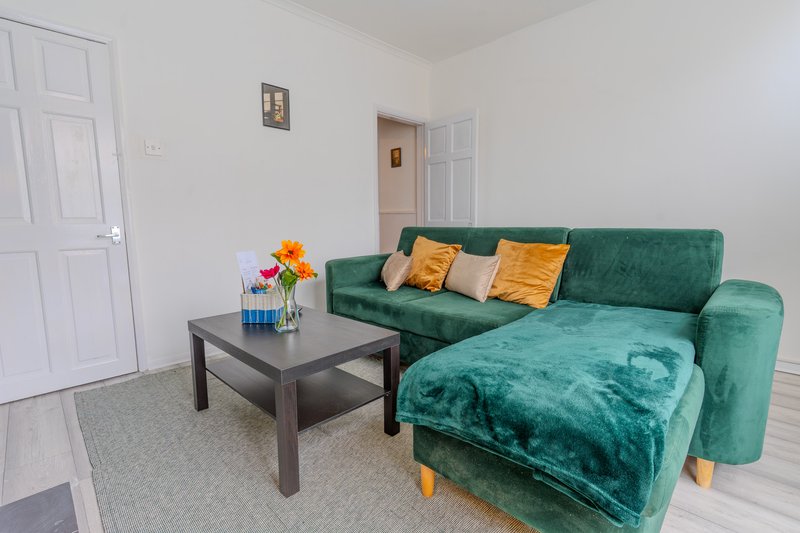 Bright living room with green velvet sectional sofa, coffee table, and colorful throw pillows