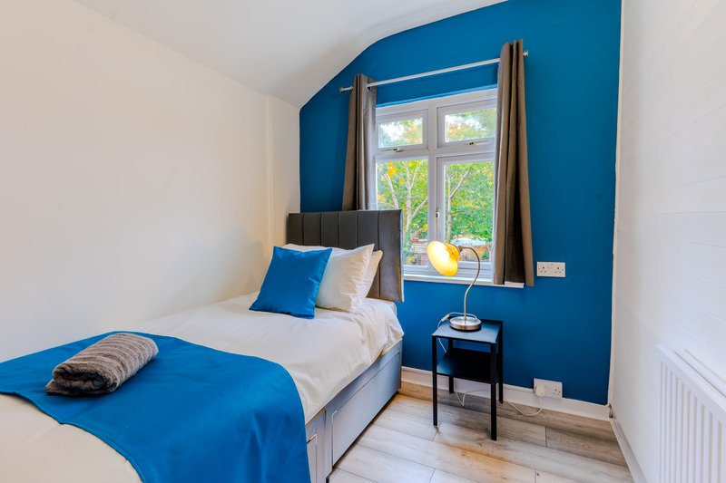 Modern bedroom with single bed, blue accent wall, window with curtains and bedside table