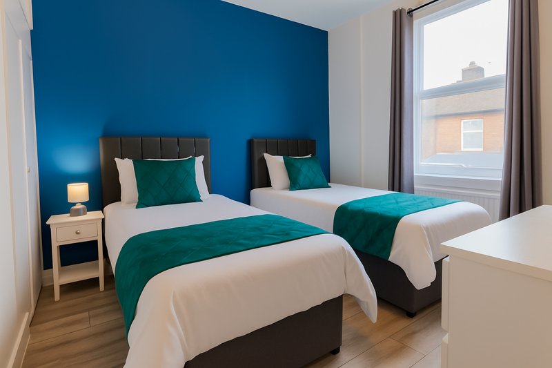 Twin bedroom with teal feature wall, two beds with green and white bedding, wooden floor and window