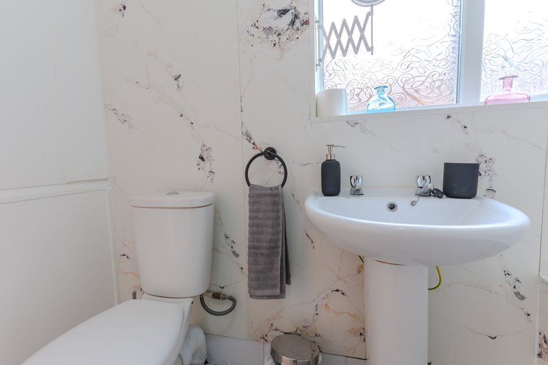 Small bathroom with toilet, pedestal sink, towel rail and window with frosted glass