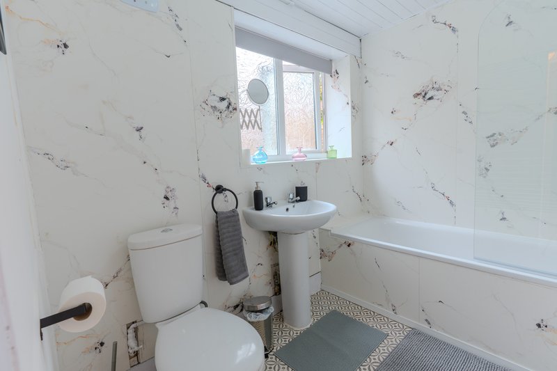 Small bathroom with toilet, pedestal sink, bathtub and patterned wallpaper