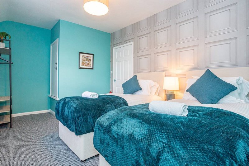 Bright bedroom with two twin beds, teal bedding, turquoise accent wall, and white wardrobe