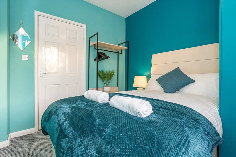 Bright turquoise bedroom with double bed, rolled towels, cream headboard, and pendant lamp