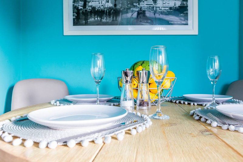 Bright turquoise dining room with set table, white plates, champagne flutes, and yellow flowers