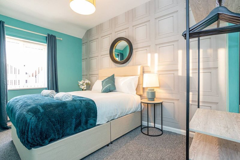 Modern bedroom with teal walls, double bed, round mirror, and metal bed frame
