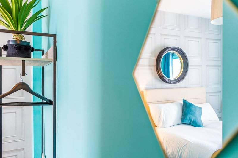 Bright turquoise bedroom with single bed, round mirror, potted plant and shelving unit
