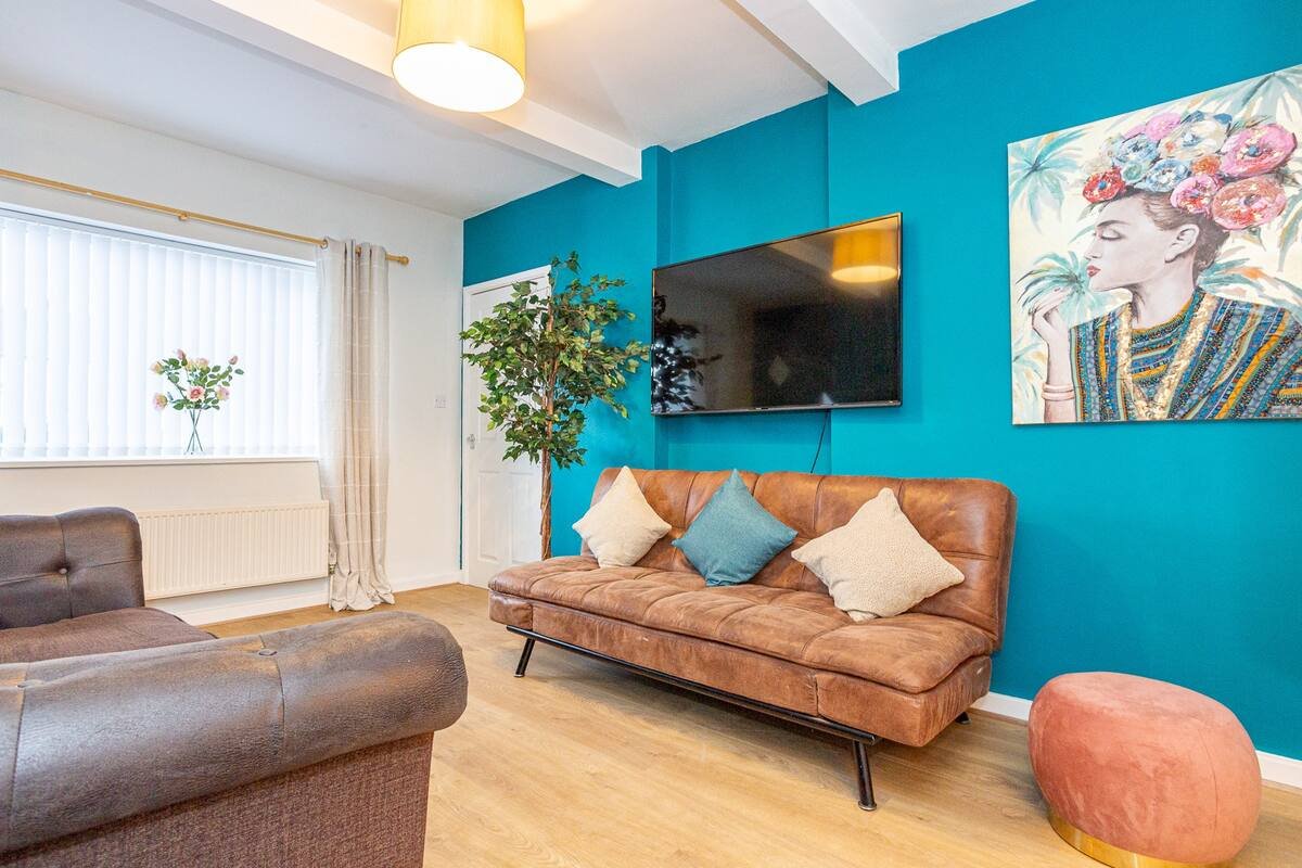 Living room with tan leather sofa, blue accent wall, TV, plants and colorful cushions