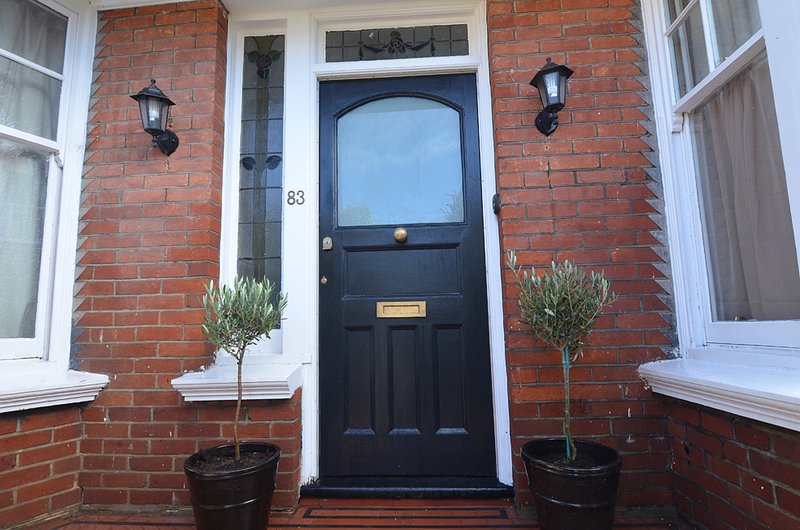 Red brick Victorian terraced house entrance with black door, number 83, and potted plants